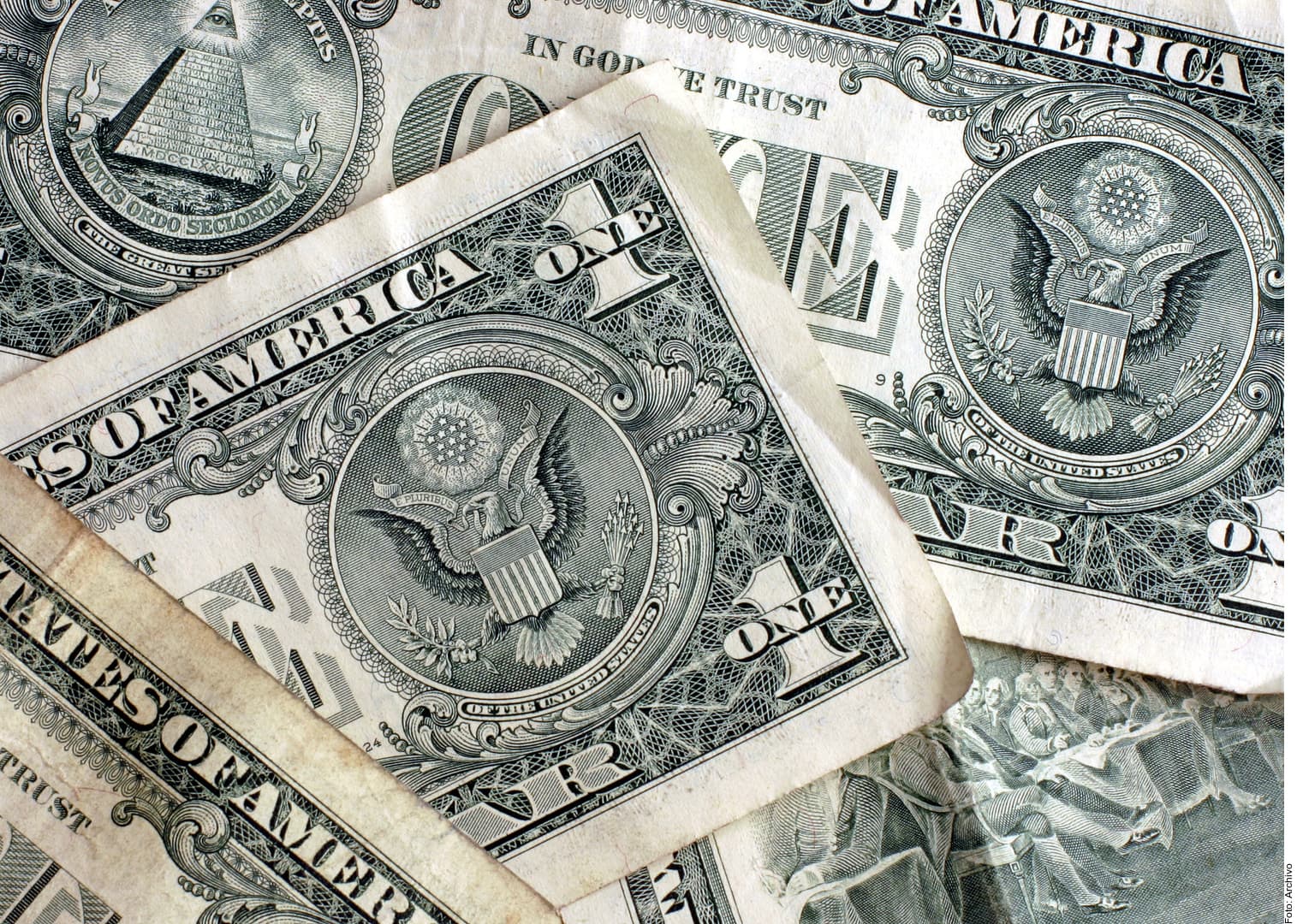 Billetes de dólar estadounidense superpuestos mostrando el águila del Gran Sello y detalles de diseño de moneda.