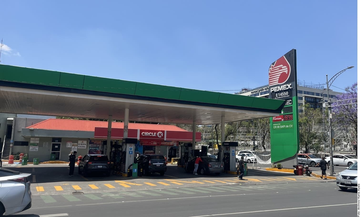 Gasolinera PEMEX con señalización de precios y clientes en las bombas de combustible.