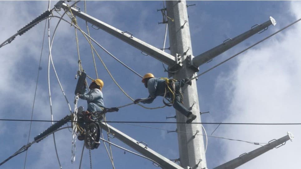 Dos trabajadores con equipo de seguridad realizan mantenimiento en cables y estructuras de una torre de distribución eléctrica.