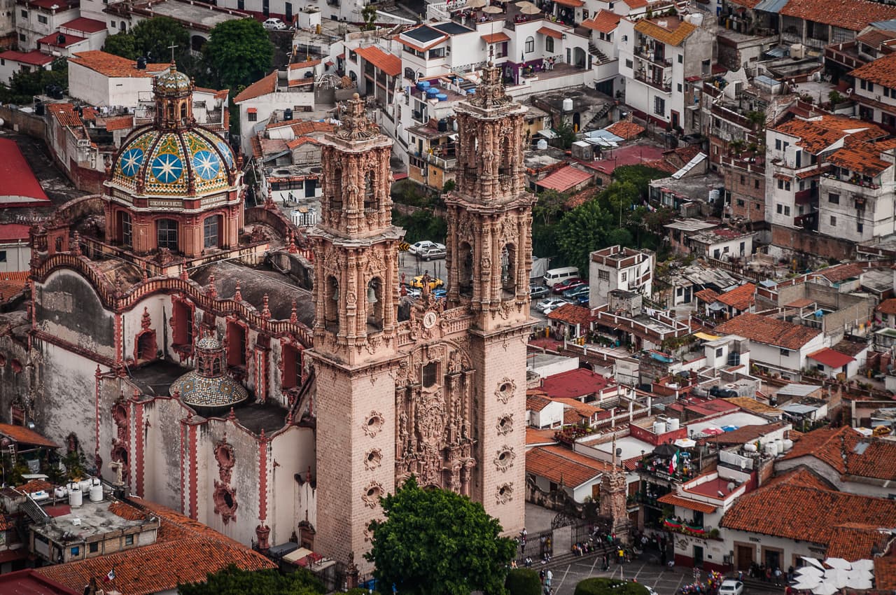 Vista aérea de una iglesia colonial con cúpula dorada y torre ornamentada rodeada de casas con techos de tejas rojas en una ciudad mexicana.