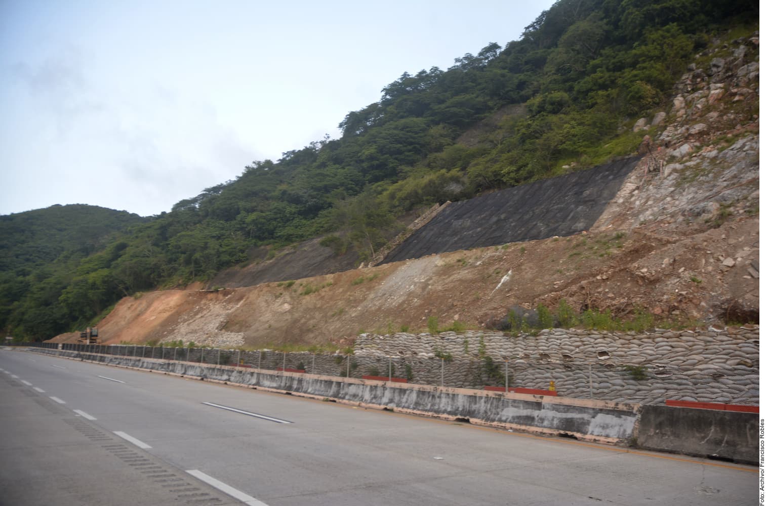 Obra de infraestructura vial en construcción con talud estabilizado, barrera de contención y maquinaria en zona montañosa.