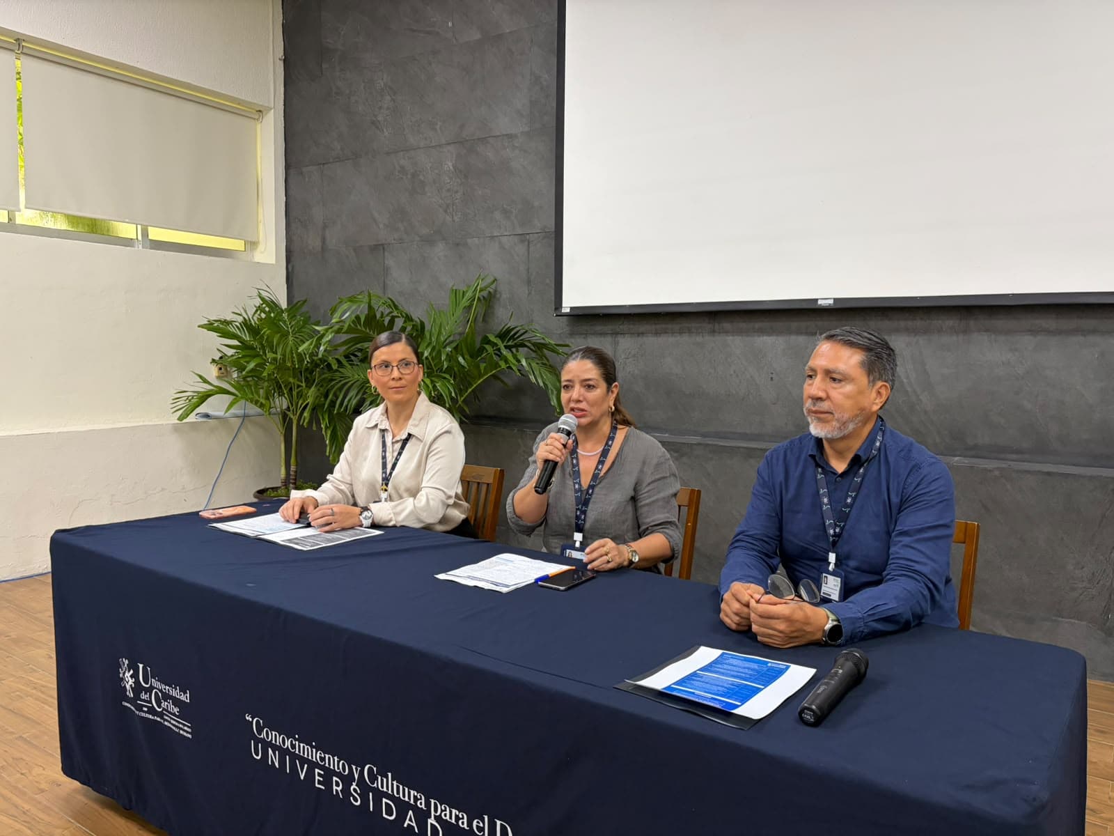 Tres panelistas en una mesa de conferencia con branding de Universidad del Caribe durante una presentación sobre tecnología e innovación.