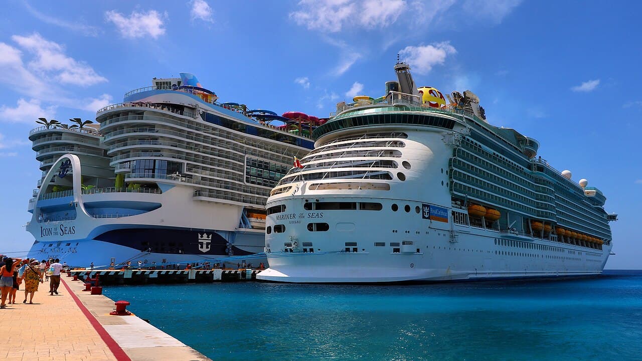 Dos cruceros de Royal Caribbean atracados en un puerto tropical con aguas turquesas y pasajeros en el muelle.