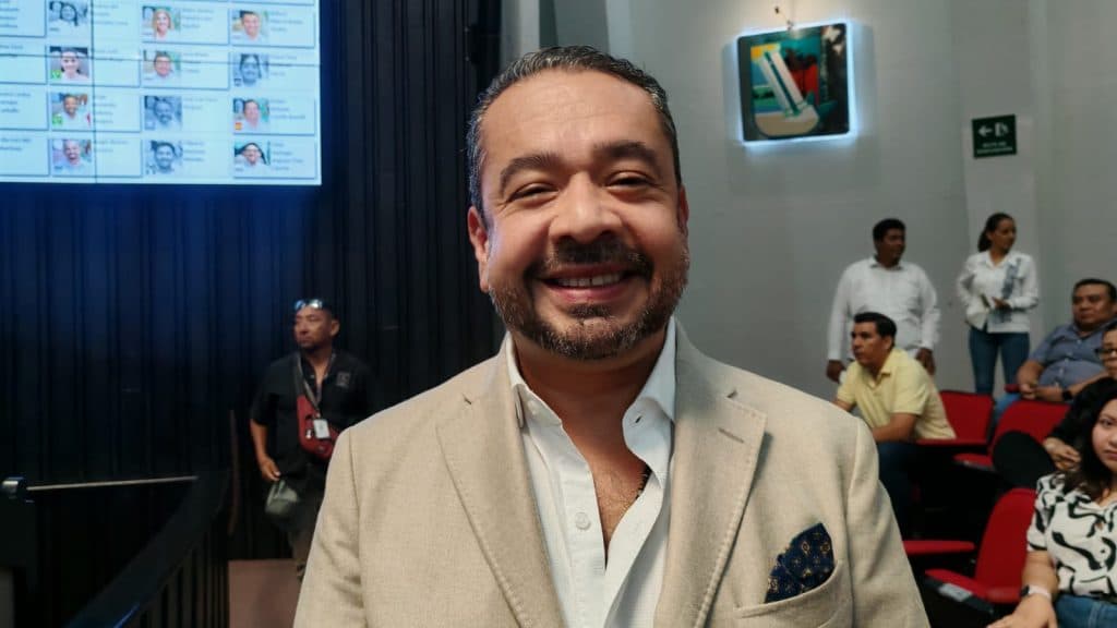 Hombre de negocios sonriendo en evento con asistentes de fondo en sala de conferencias.