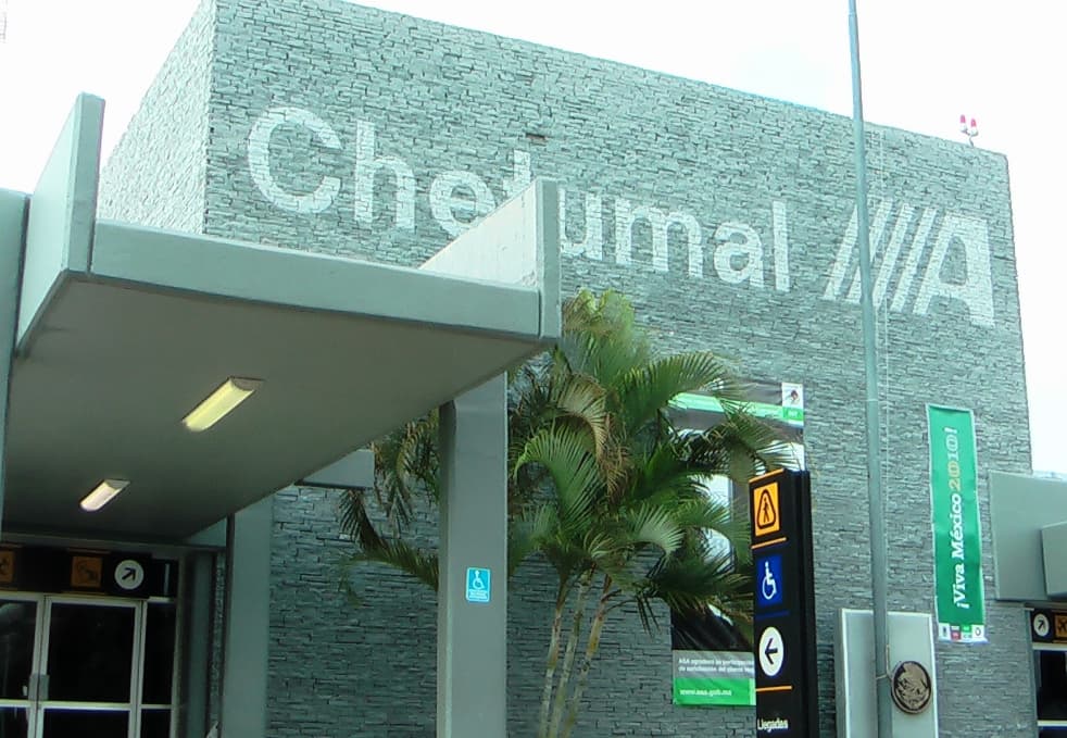 Fachada moderna del Aeropuerto Internacional de Chetumal con señalética de accesibilidad y vegetación tropical.