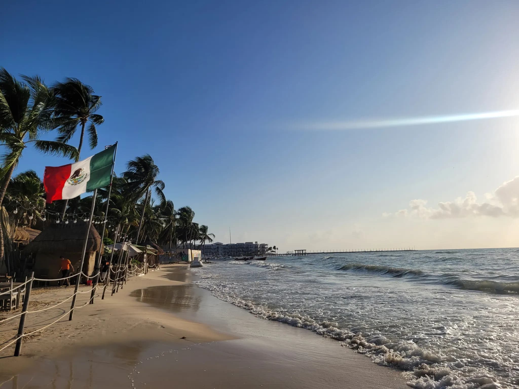 Playa de Playa del Carmen con palmeras y una bandera de México junto al mar